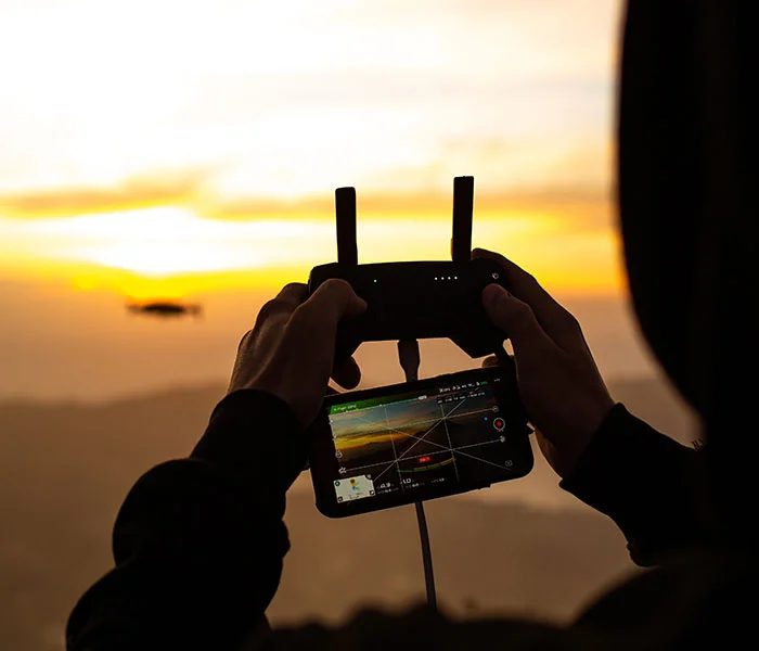 Person flying a drone at sunset with a controller and live video feed.